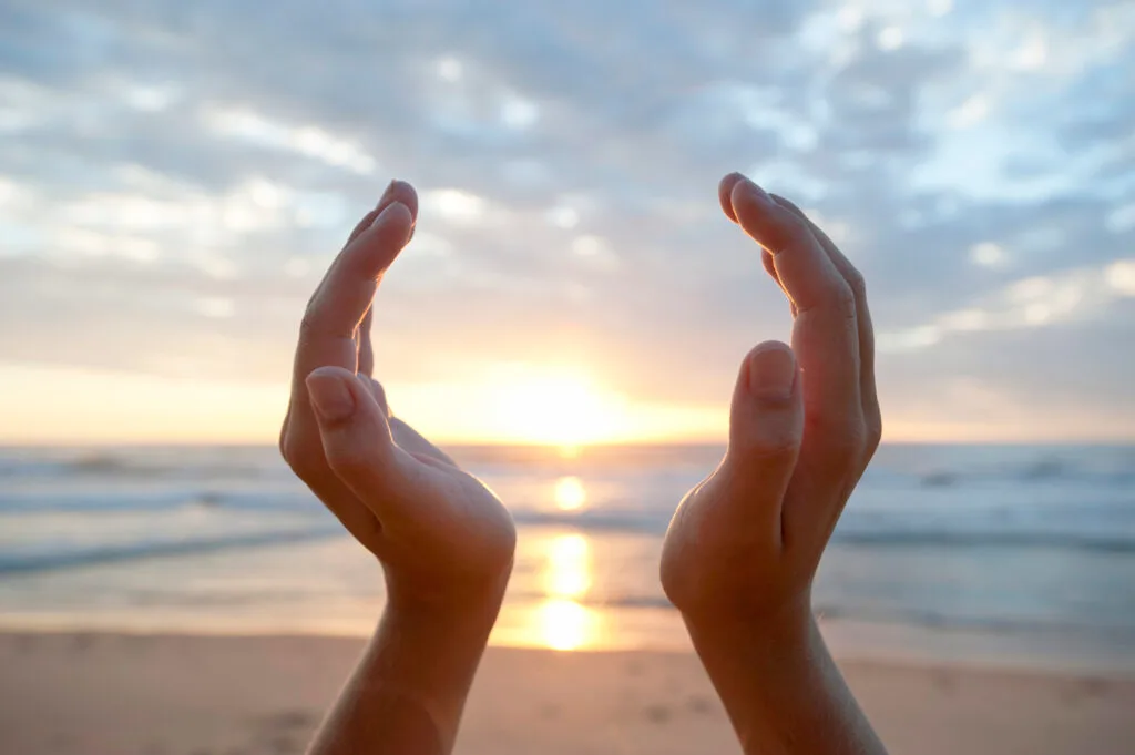 Two hands cupped around the setting sun on a beach