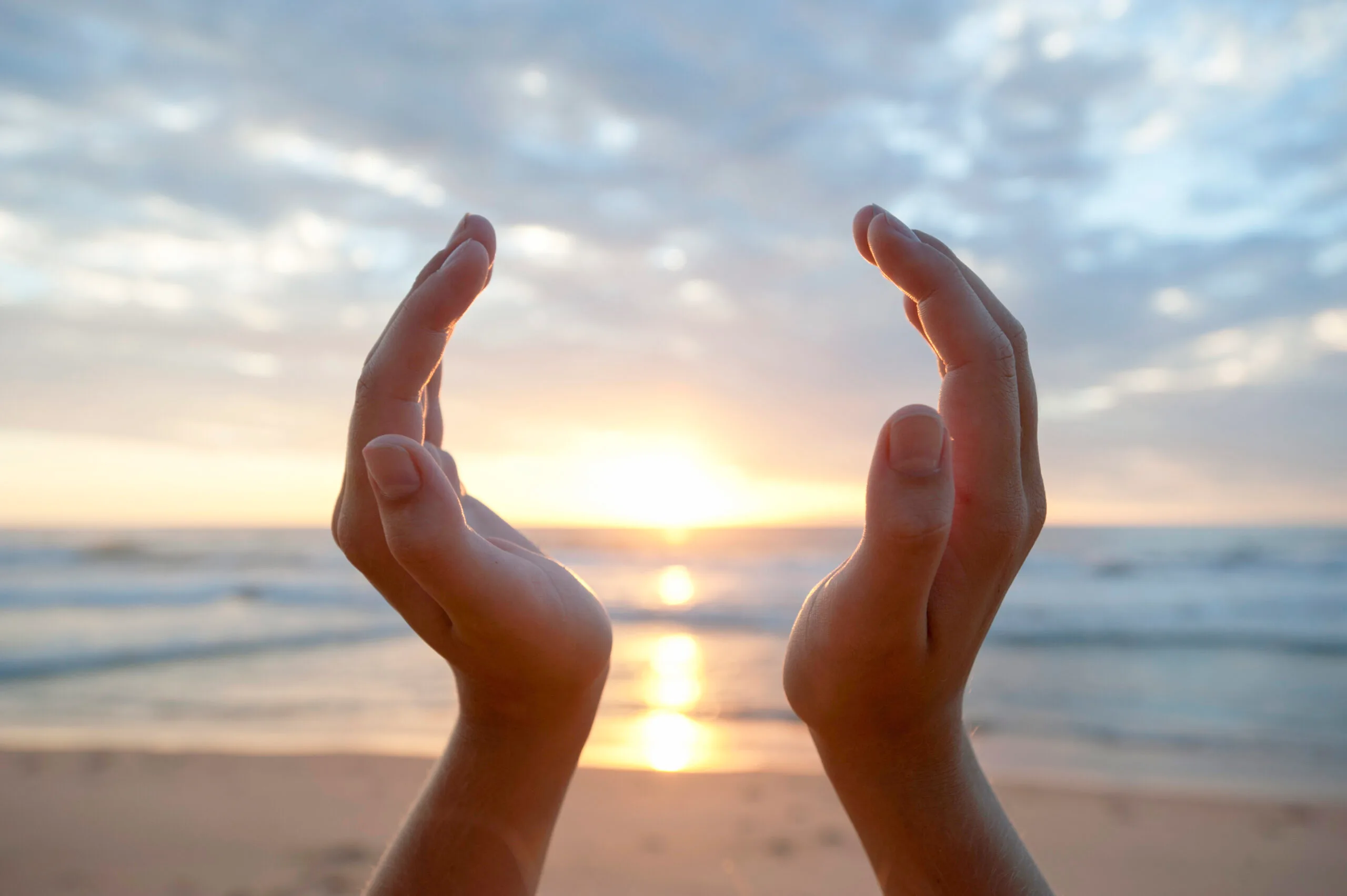 Two hands cupped around the setting sun on a beach