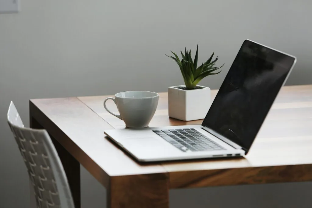 A laptop, cup of tea and small plant on a desk, set up for an online counselling or coaching session